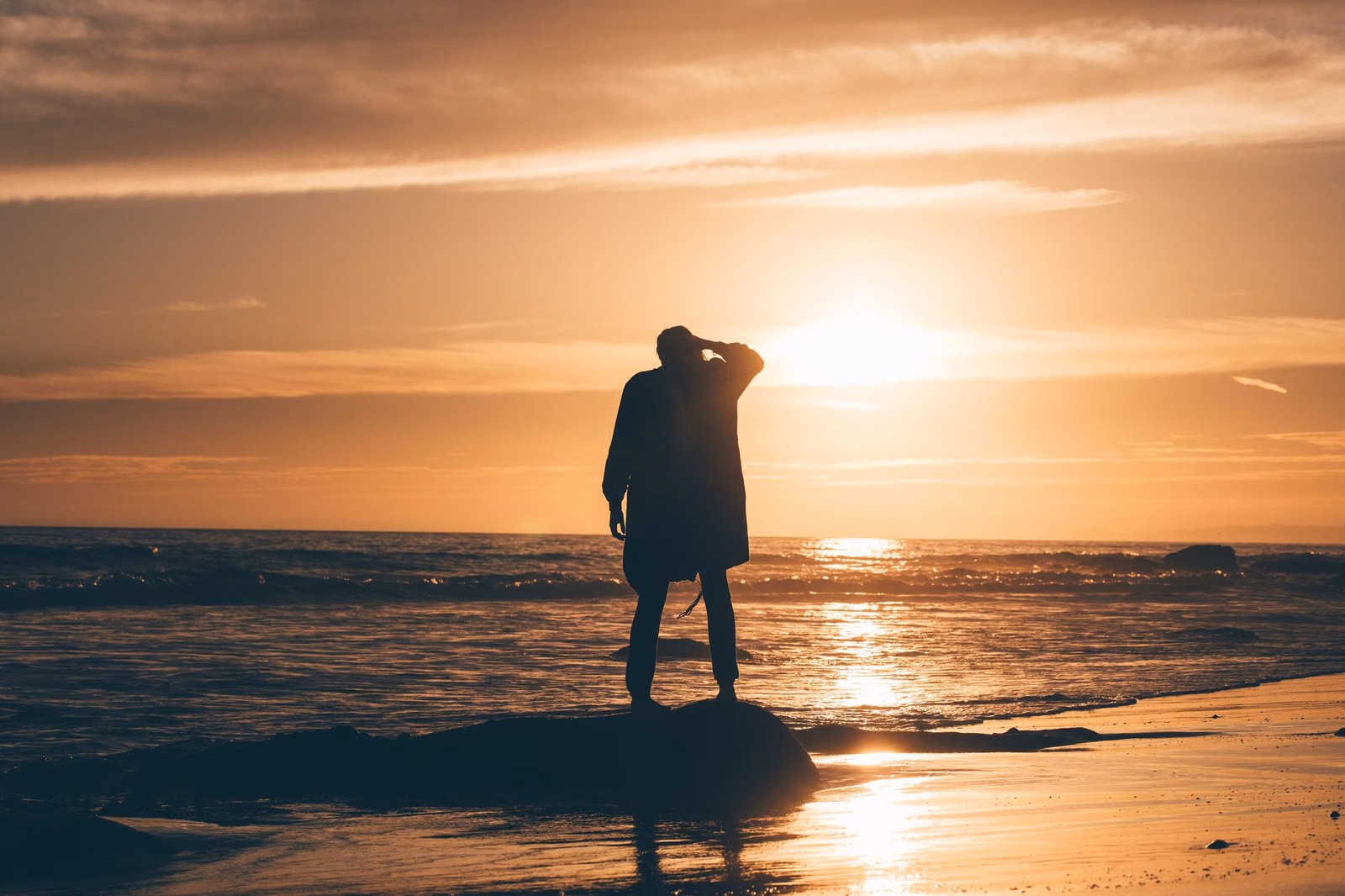 A person silhouetted at the shoreline against an orange sunset in Malibu